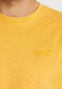 Žluté bavlněné tričko s kulatým výstřihem a krátkými rukávy. Na hrudi se nachází výšivka loga "Levi's" ve stejné žluté barvě. Hladká textura.