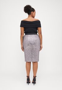 Melnas plecu atklājošas blūzes apģērbs, kas kombinēts ar ceļgala garuma sudrabaini mirdzošu zīmuli svārku. Stiletto papēži papildina apģērbu.