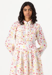 Φόρεμα με φλοράλ σχέδιο σε παστέλ χρώματα, με ραμμένο κορσέ, μακριά μανίκια και γιακά με κουμπιά. Κατασκευασμένο από ελαφρύ ύφασμα, με πλισέ φούστα.