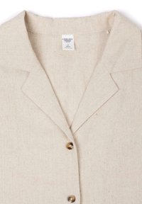 Light beige button-up shirt made of textured fabric with a collared neck and two brown buttons down the front. Label visible inside.