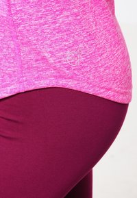 Rosa heathered träningsöverdel med korta ärmar och logodetalj, kombinerad med figurnära vinröda leggings. Texturen verkar slät och elastisk.