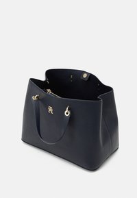 Borsa tote in pelle blu navy con superficie texture, dettagli in metallo dorato e apertura superiore. Presenta un logo sul fronte e manici doppi.