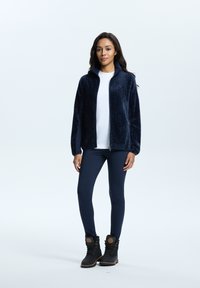 Navy gebreid fleecejack met een rits, gecombineerd met een wit T-shirt en navy legging. Zwarte laarzen met een bontrand en veters.
