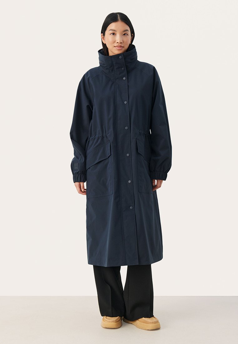 Cappotto lungo da marinaio realizzato in materiale resistente all'acqua, caratterizzato da un colletto alto, chiusure a scatto e due tasche frontali con vita elasticizzata.