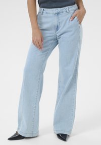 Light blue high-waisted wide-leg jeans made of denim, featuring a front pocket and stitched seams, paired with pointed black shoes.