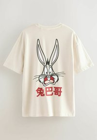 Cremfarbendes T-Shirt mit einem Grafikdesign eines Cartoonkaninchenkopfes mit großen Ohren und rotem Text darunter in fetter Schrift.
