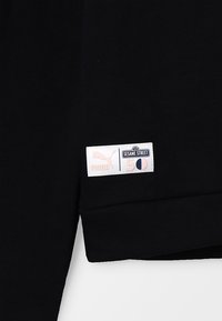 Tessuto nero con un'etichetta bianca e rosa con le scritte "PUMA", "SESAME STREET" e "50". Il design presenta una linea semplice e classica.