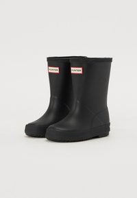 Bottes de pluie en caoutchouc noir avec une texture lisse, dotées d'étiquettes "HUNTER" rouges et blanches à l'avant et d'une semelle noire texturée.
