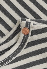 Black and white striped fabric with close-up of a seam and copper rivet featuring a four-leaf clover design.