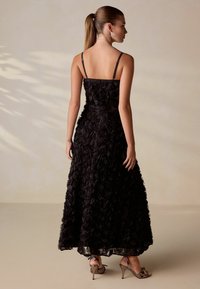 Černé květinové maxi šaty s 3D aplikacemi růží, nastavitelnými ramínky, volnou sukní a párem sandálů s kovovými pásky.