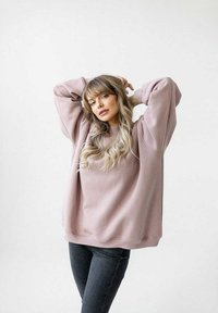 Przesadnie wielka, jasnoróżowa bluza z opadającymi ramionami i ściągaczami, w połączeniu z ciemnymi dżinsami. Miękka tkanina z minimalną ilością szwów.