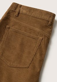 Tissu en velours côtelé marron avec des rainures verticales visibles, montrant une poche arrière et des passants de ceinture sur un pantalon.