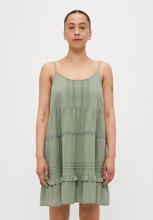 Vihreä hihaton mekko, jossa on istuva yläosa ja röyhelöhame. Koristeltu tekstuurikuvioilla ja pitsiaksenteilla. Pehmeä kangas, joka istuu mukavasti.