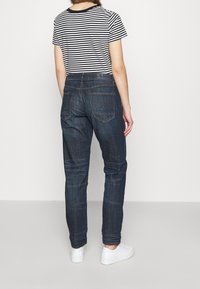 Tmavě modré džíny s volným střihem, se dvěma zadními kapsami a jemnou texturou. V kombinaci s černobílým pruhovaným tričkem a bílými teniskami.