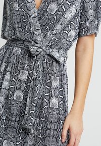 Vestido de estampado de serpiente en blanco y negro, con mangas cortas, un escote en V profundo y un lazo en la cintura, que presenta una tela texturada y tejida.