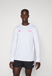 Long-sleeve white shirt with pink graphics, including "BMW Berlin Marathon," and black Adidas logo accents. Soft cotton material, fitted design.