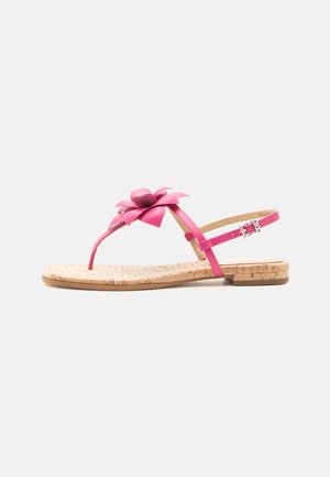 Rosa flache Sandale mit Korksohle, Zehensteg, Blumenverzierung oben und verstellbarem Knöchelriemen mit Schnalle auf weißem Hintergrund.