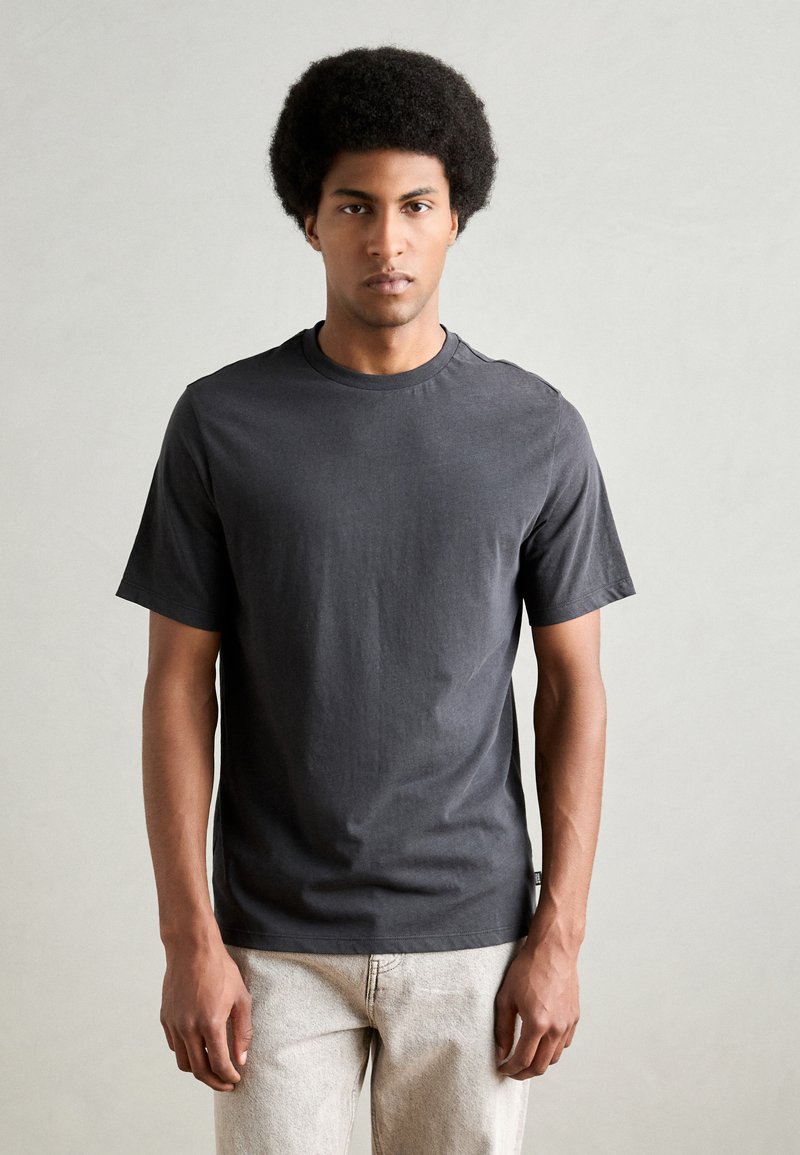 T-shirt à col rond gris foncé en coton doux avec des manches courtes, présentant une coupe décontractée et des détails de couture subtils.