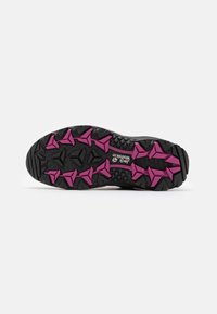 Semelle de chaussure de trail noire et rose présentant une surface texturée avec des crampons en forme de triangles et de flèches pour l'adhérence et la stabilité.