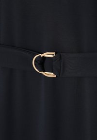 Fekete vászonöv arany dupla gyűrűs csattal, amely sötét, az övvel megegyező ruhát szorít össze.