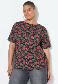 Czarna koszula z krótkim rękawem z kwiatowym wzorem przedstawiającym czerwone róże i zielone liście. Luźny krój z okrągłym dekoltem, zestawiona z szarymi dżinsami.