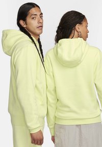 Hoodie giallo neon realizzati in tessuto morbido, caratterizzati da una tasca frontale, cappuccio con cordino e polsini a coste. Una persona è rivolta in avanti, l'altra all'indietro.