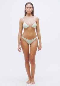Σετ μπικίνι ανοιχτού πράσινου με τριγωνικό πάνω μέρος και σλιπ χαμηλής μέσης. Ομαλή υφή, λεπτές τιράντες, μινιμαλιστικός σχεδιασμός και χωρίς ορατά μεταλλικά στοιχεία.