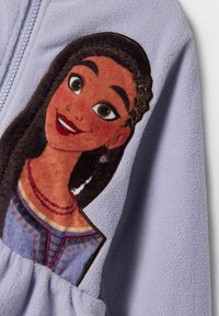 Fleecejacka i lavendel med en texturerad, färgglad applikation av en karaktär, med detaljerade ansiktsdrag och flätade håraccenter.