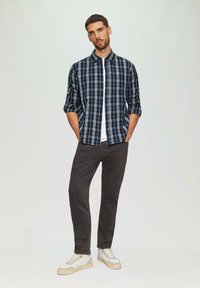 Marine ruitjes overhemd met witte lijnen, opgerolde mouwen, gecombineerd met donkergrijze broek en lichte sneakers met beige accenten.