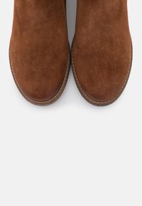 Brown suede ankle boots with rounded toes, contrasting stitching, and a smooth texture. The sole is slightly raised.