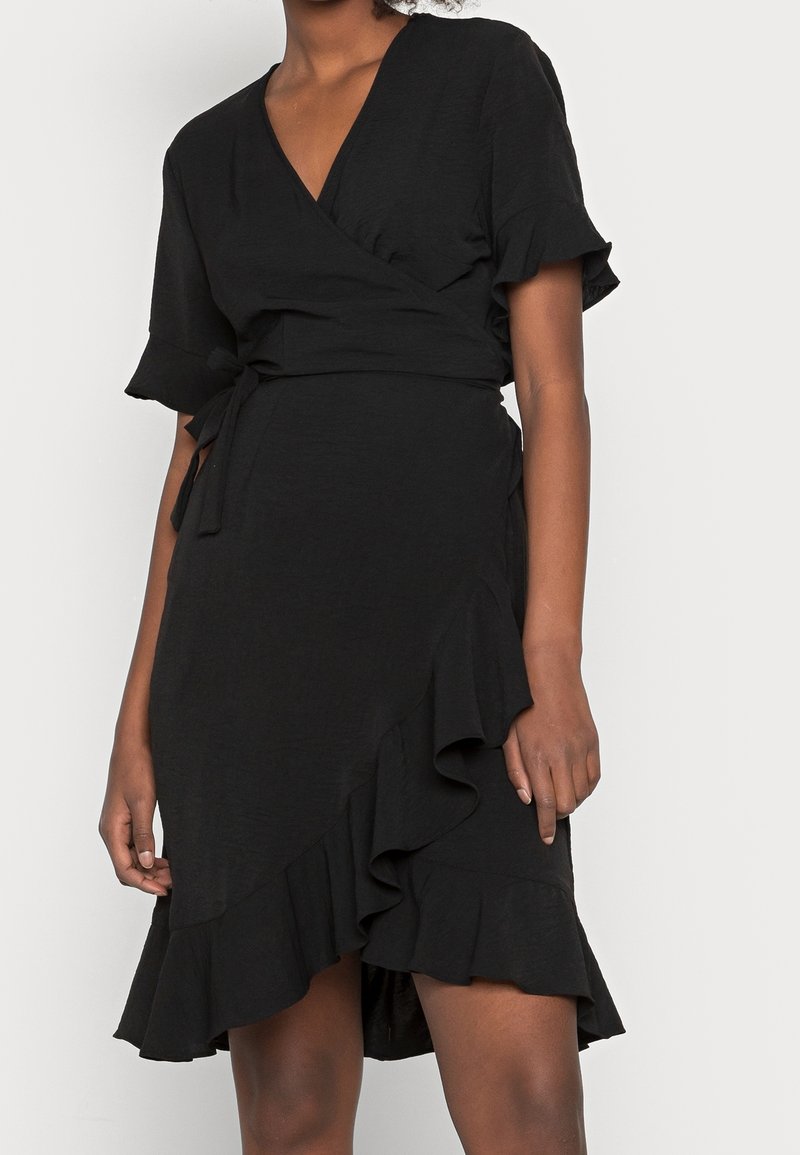 Vestido negro envolvente de tela ligera, con mangas cortas acampanadas y un dobladillo con volantes, además de un detalle de cintura atada.