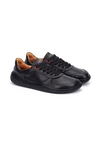 Zapatillas de cuero negro con punta redonda, acentos perforados, ojales rojos en contraste y una suela de goma texturizada. Forro interior marrón.