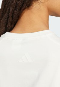 Weißes Baumwoll-T-Shirt mit Rundhalsausschnitt. Hat ein erhabenes, weißes Adidas-Logo auf der Rückseite, das eine glatte, weiche Textur zeigt.