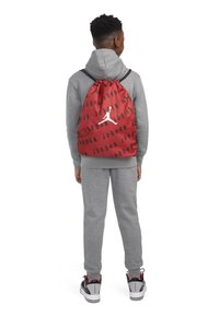 Crvena torba s uzicom s crnim uzorkom "JORDAN", s bijelim Jumpman logom, pričvršćena za sivi duksericu i trenirke.