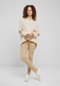 Beige knit sweater with long sleeves and star patterns on cuffs, paired with beige cargo pants and white sneakers, set against a neutral background.