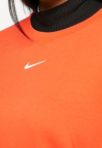 Orange sweatshirt med ett ribbade svart hög halsringning, med en liten vit Nike-logotyp på framsidan. Mjuk tygstruktur.