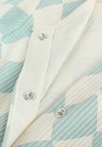 Könnyű anyag közeli képe, menta zöld és törtfehér mintázattal, ezüst nyomógombokkal és bordázott textúrával.