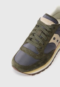 La chaussure présente un dessus en daim vert foncé et en tissu bleu marine, des lacets ronds, une semelle en caoutchouc beige, et un accent logo beige sur le côté.