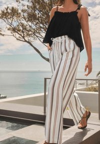 Black, off-the-shoulder top with ruffled trim, paired with white trousers featuring vertical red and navy stripes, tied at the waist.