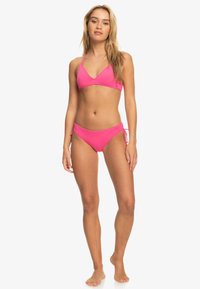 Felle roze bikini set met een driehoek top met dunne bandjes en bijpassende zij-tie onderbroekjes. Gladde, rekbare stof met minimale bedekking.