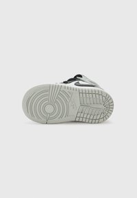 Baskets avec une semelle en caoutchouc blanc texturé, des accents noirs et un motif circulaire distinct. Présente un dessus lisse dans une palette de couleurs grises.