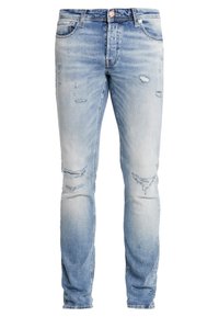 Jeans de mezclilla azul claro con un corte ajustado, detalles desgastados en los muslos y las rodillas, diseño de cinco bolsillos y acentos de hardware en tono dorado.