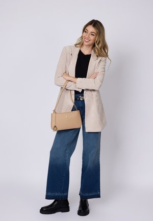 Blazer de pana beige, top negro, jeans de mezclilla azul de pierna ancha, botas negras hasta el tobillo y un pequeño bolso de hombro beige con cadena.