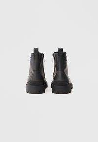 Botine negre din piele cu talpă masivă, dotate cu închidere cu fermoar, mânere pentru încălțare și un logo embosat pe partea din spate. Design minimalist.