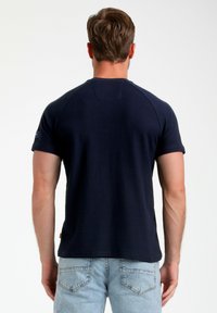 T-shirt blu navy a maniche corte con scollo a girocollo e dettagli di cucitura sulla schiena, abbinato a jeans in denim chiaro.