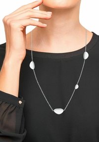 Zilveren ketting met vijf gladde, druppelvormige accenten van verschillende maten; gepresenteerd tegen een zwarte top.