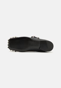Zapato de cuero negro con una superficie lisa, suela plana y clavos metálicos decorativos a lo largo del talón. Diseño minimalista con un acento de hebilla.