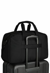 Μαύρη τσάντα duffel ασφαλισμένη στη λαβή μιας μαύρης σκληρής βαλίτσας με επεκτεινόμενη τηλεσκοπική λαβή.