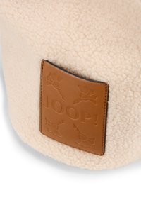 Tessuto in peluche color crema con una patch in pelle che mostra il logo "JOOP!" intagliato e un motivo decorativo, offrendo una finitura morbida e testurizzata.