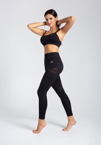 Czarny dopasowany stanik sportowy i legginsy, z perforowanymi wzorami, bezszwowym designem oraz elastycznym materiałem zapewniającym komfort i swobodę ruchów.